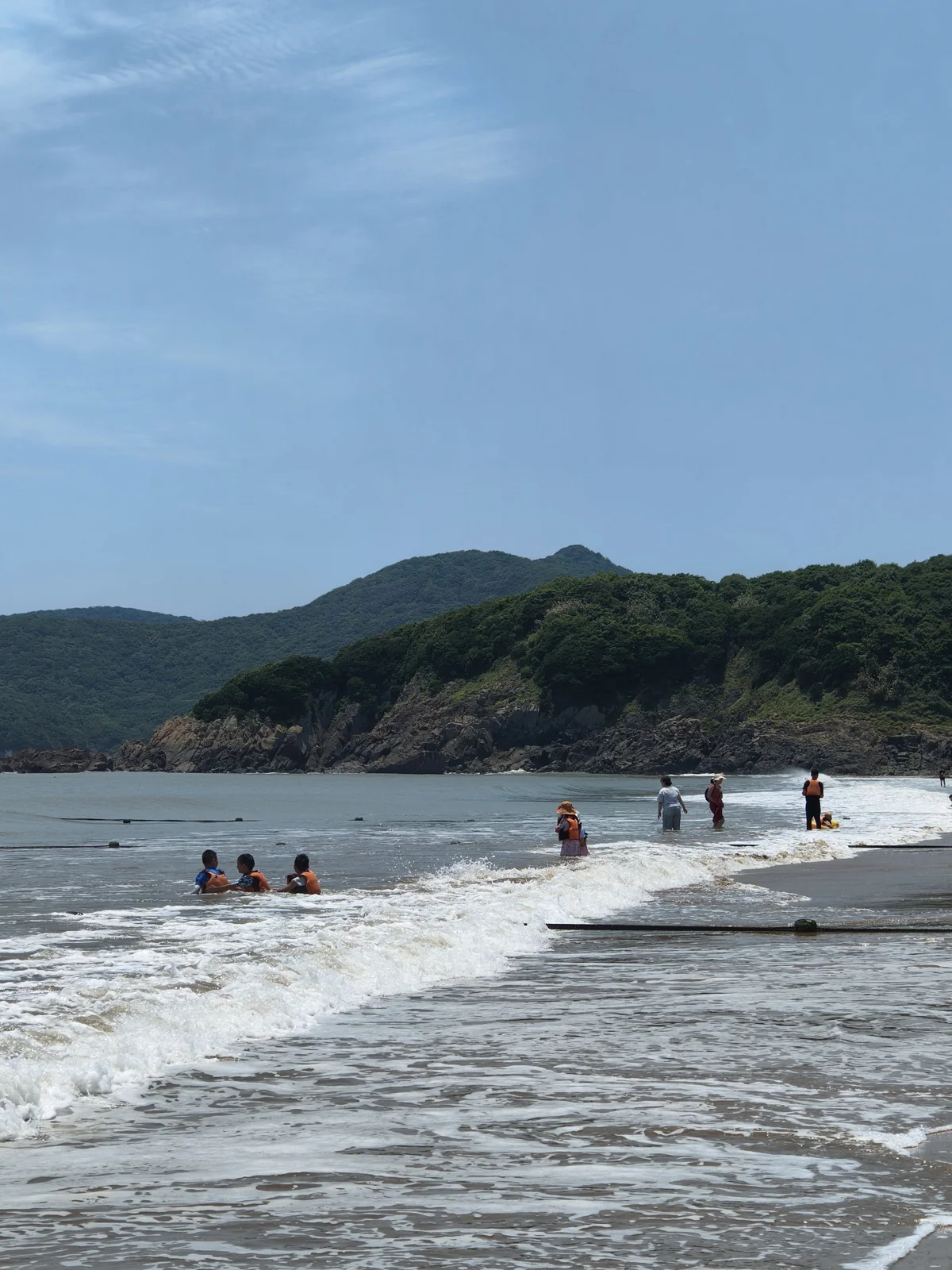 海浪拍向南沙海滩岸边，几位游客在水中游玩