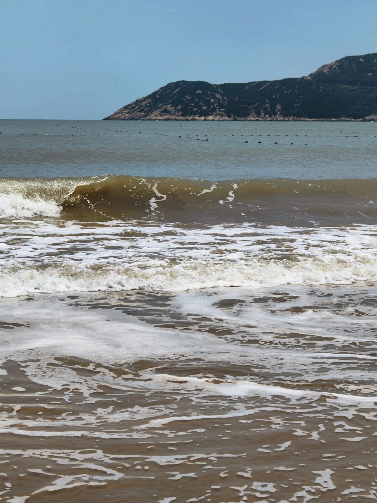 南沙海滩的近岸海水裹挟泥沙，呈现黄褐色，远处是海岛山丘