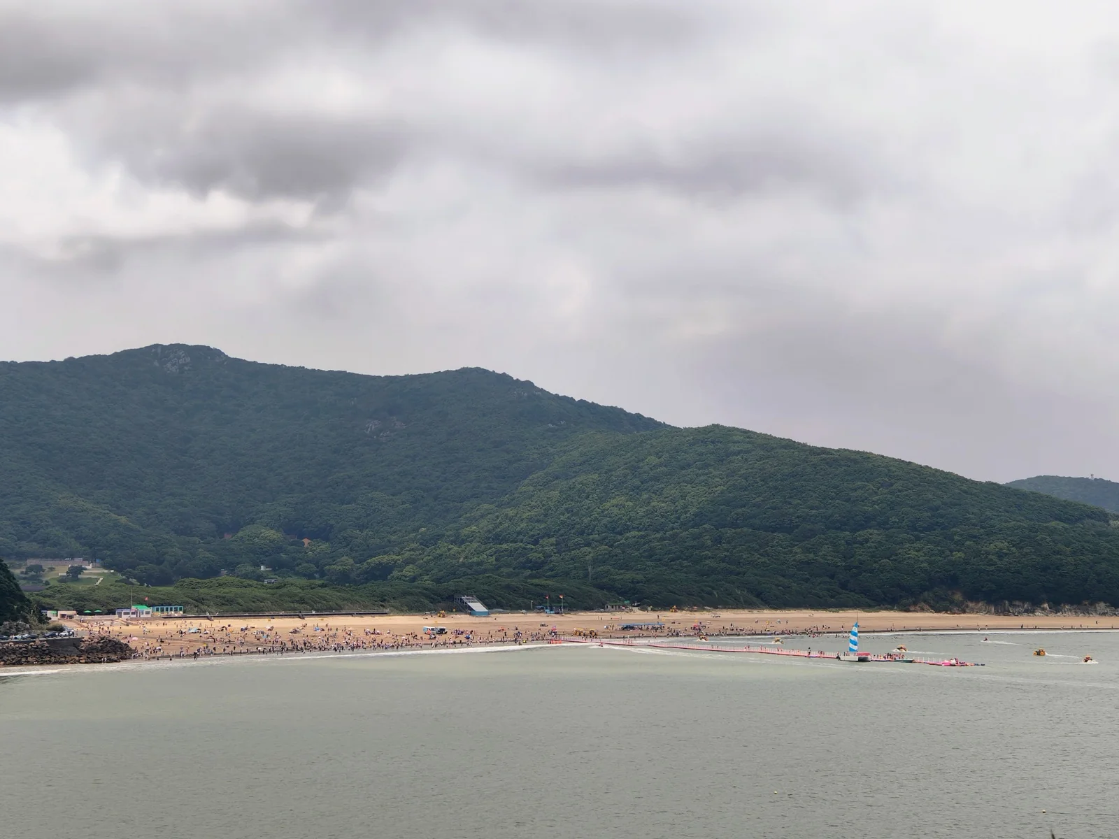 大青山沙滩全景，游客遍布，远处山峦起伏