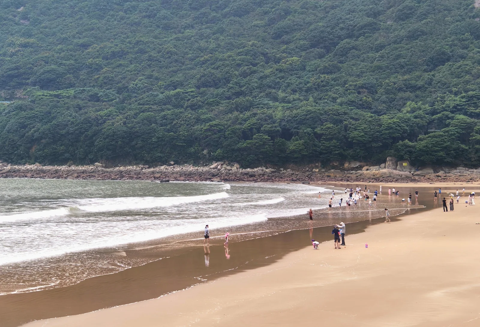 大青山景区的一处沙滩，游客众多，背后是郁郁葱葱的山林