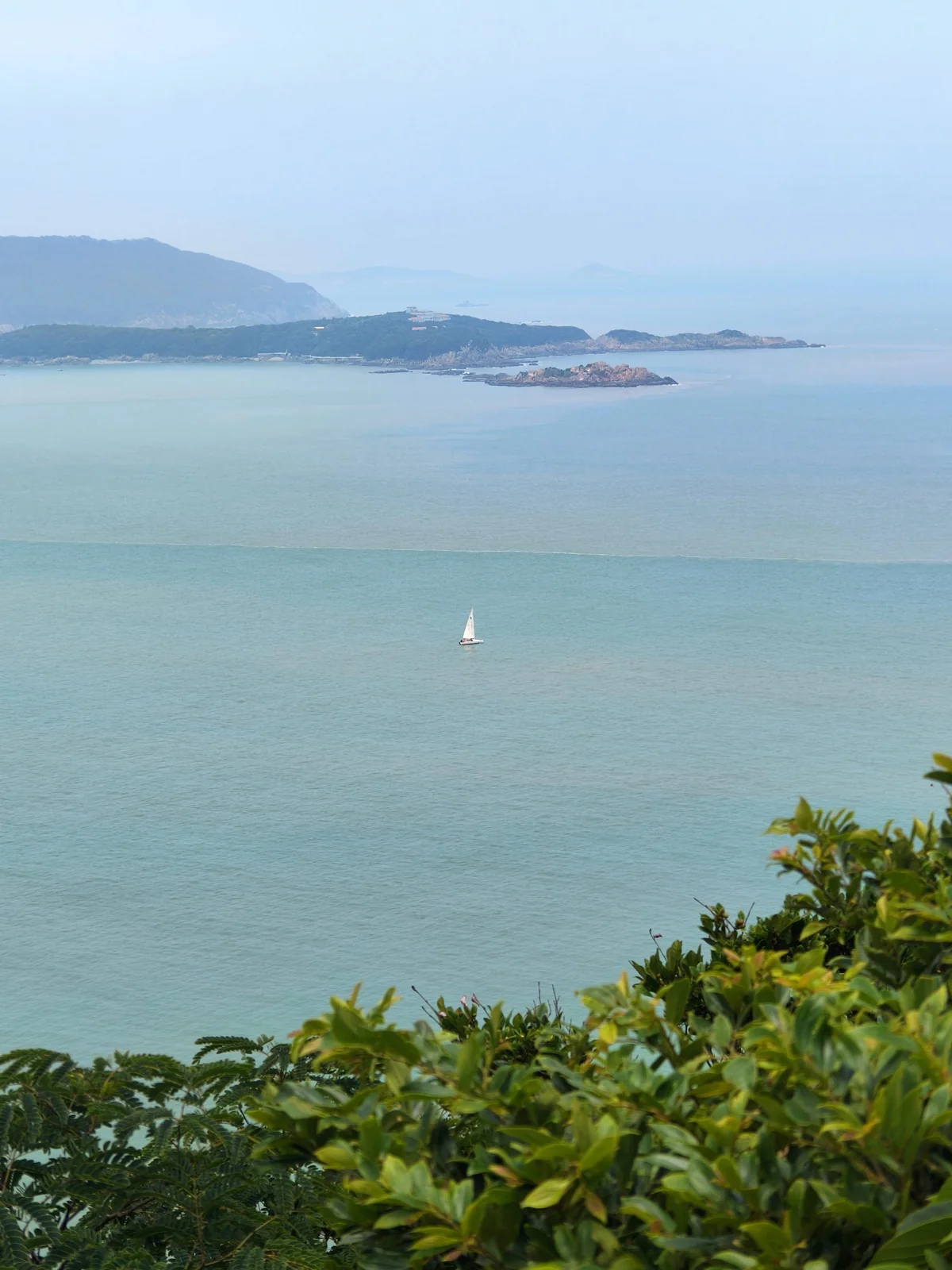 大青山远眺海面，一艘帆船点缀在平静的海面上