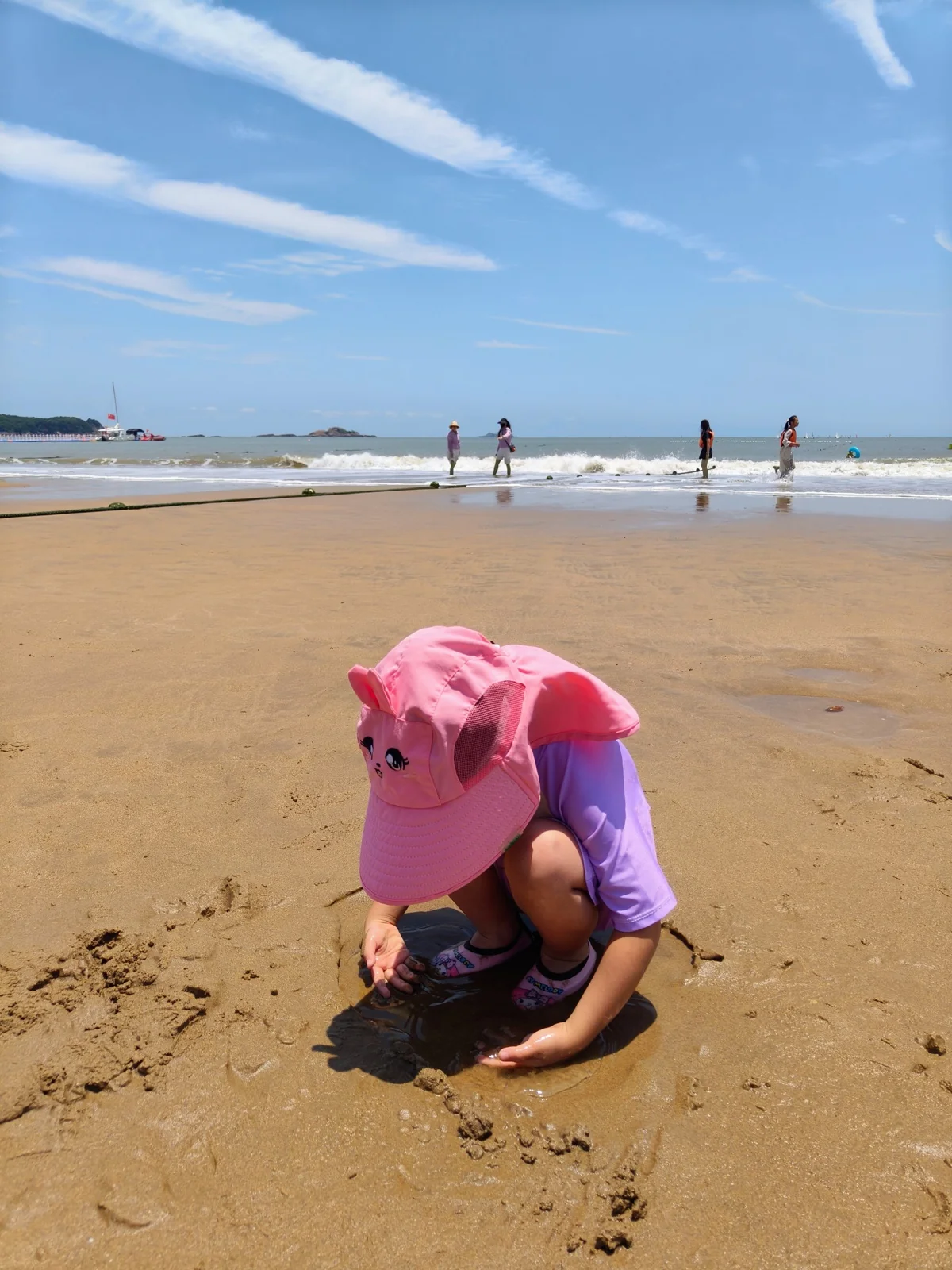 戴着粉色遮阳帽的小女孩在南沙海滩的湿沙上玩水