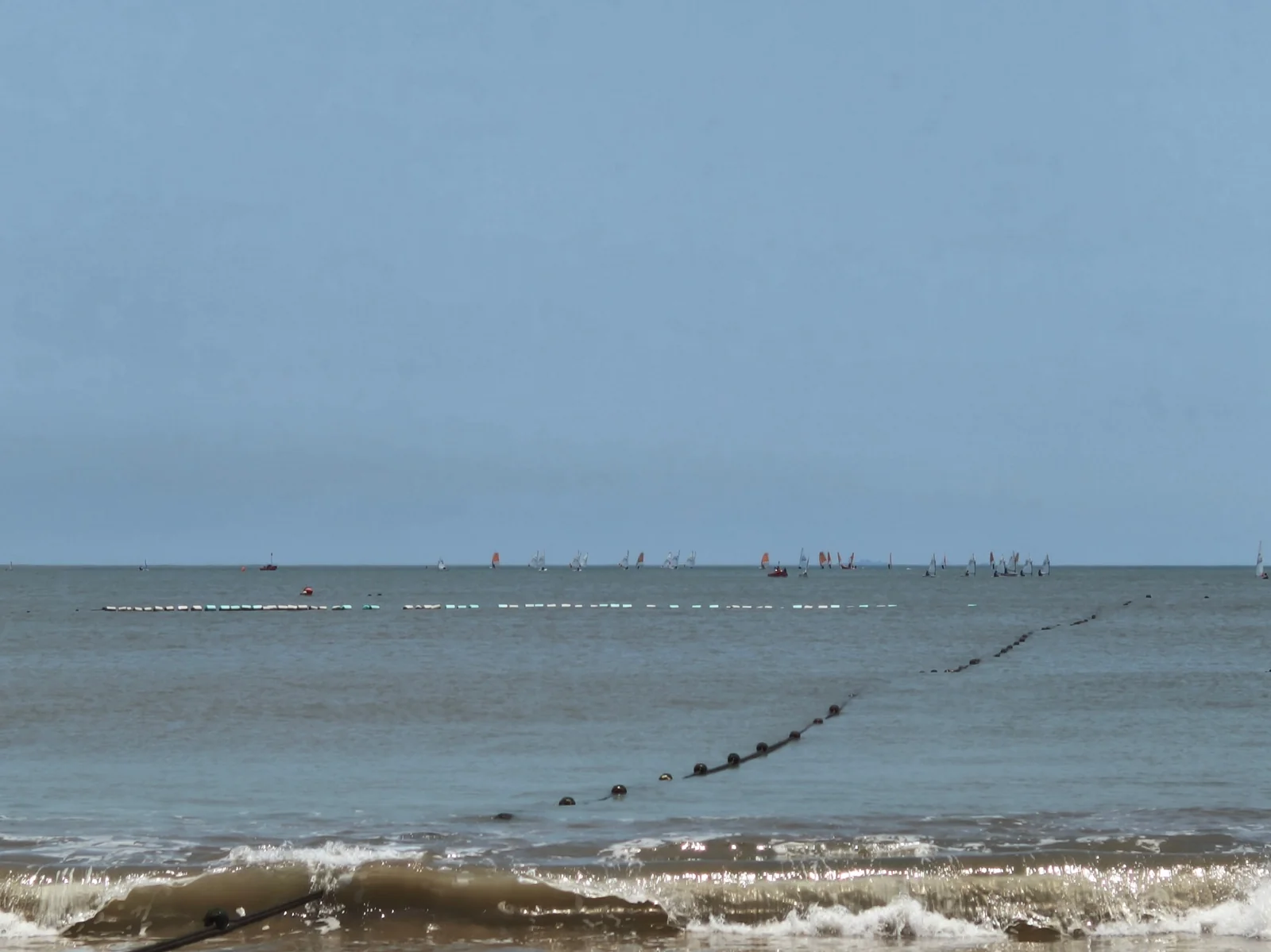 南沙海滩海面，近岸有游客在戏水，远处可见帆船与浮标