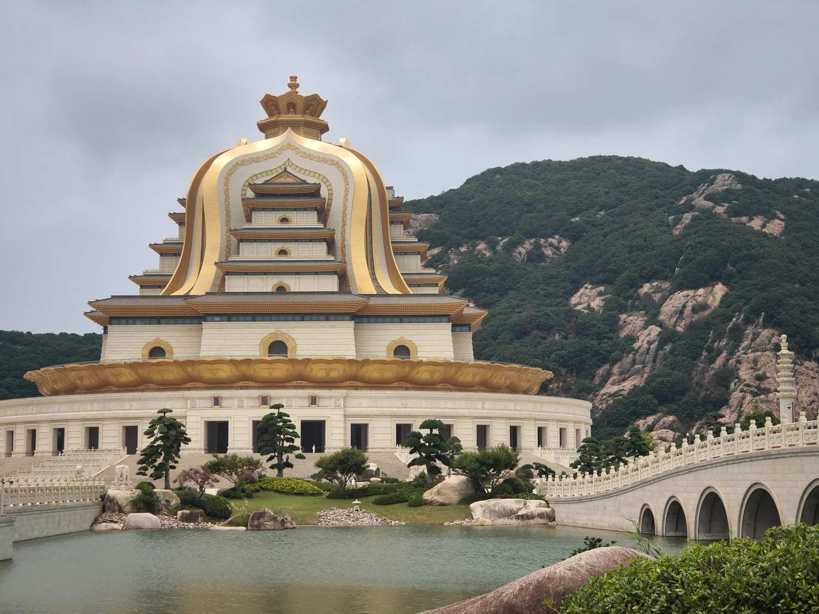 观音法界主体建筑，金色穹顶与白色塔身依山而建，前有拱桥与水面