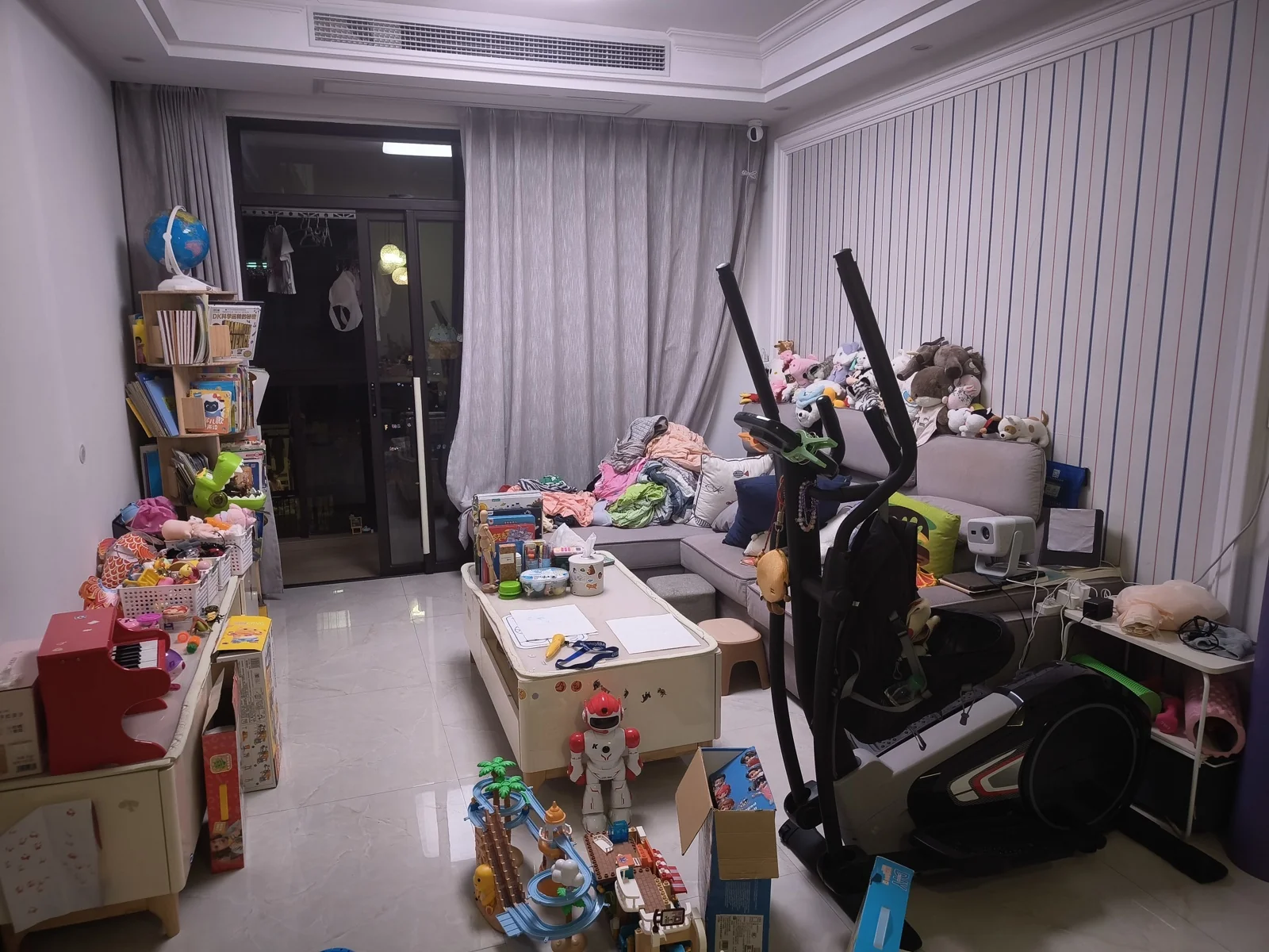 改造前堆满书籍玩具、衣服和健身椭圆机的杂乱客厅