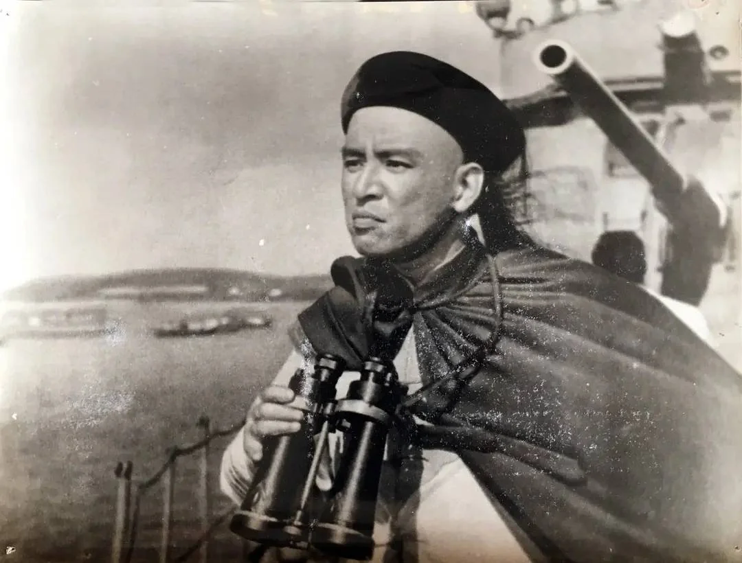 Black-and-white still of a Qing naval officer with binoculars on deck, a long gun beside him.