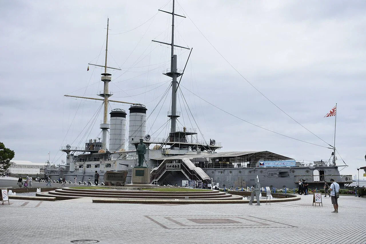 Preserved battleship Mikasa in a park dry berth, with a bronze statue on the plaza in front.