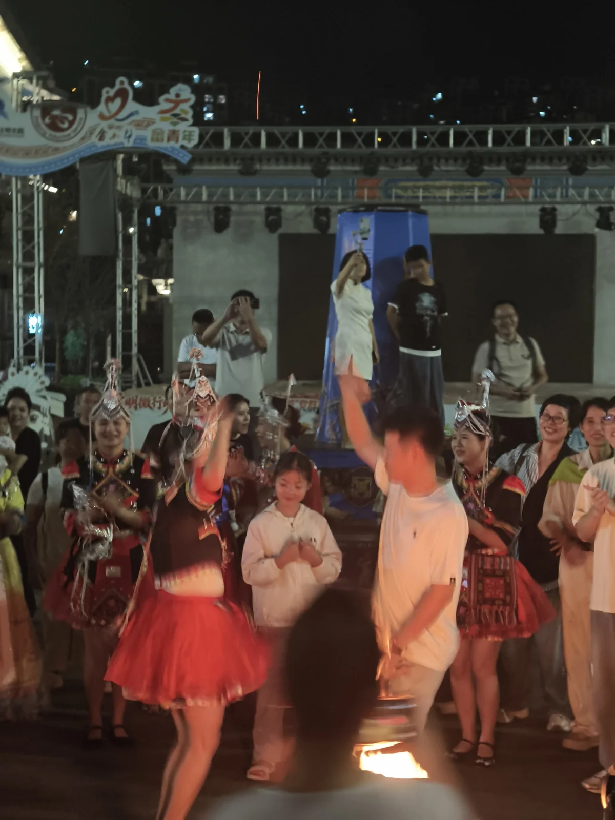 夜间舞台前，演员与游客围成圈跳舞，一旁有女孩驻足观看