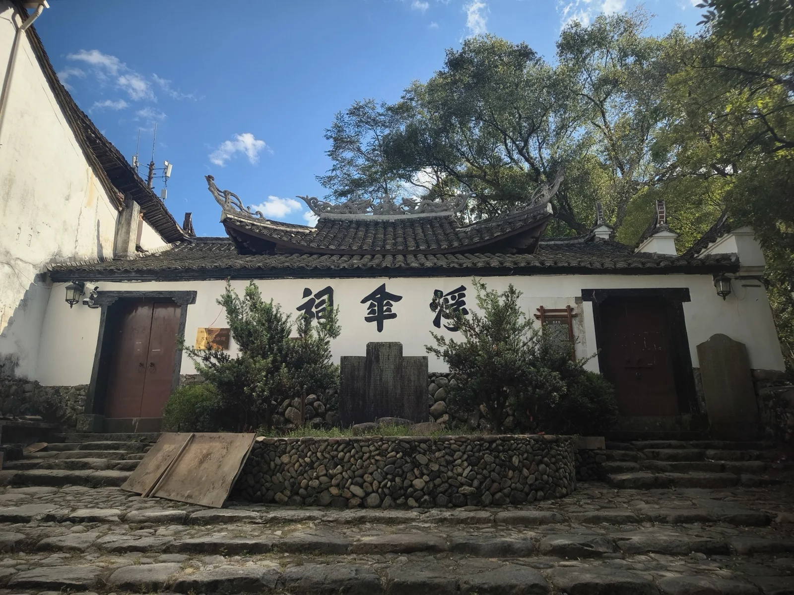 白墙黑瓦的祠堂式建筑，屋脊两端翘起，墙面题着三个墨色大字，门前是卵石台阶