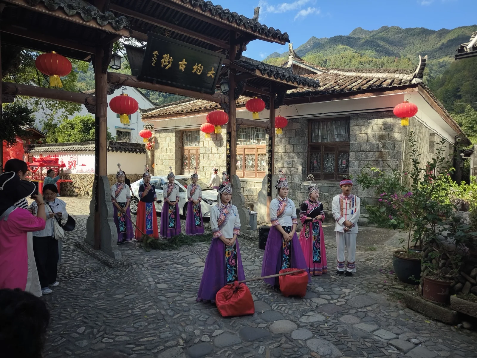 大均古街牌坊下站成两列的畲族演员和游客，檐下挂满红灯笼