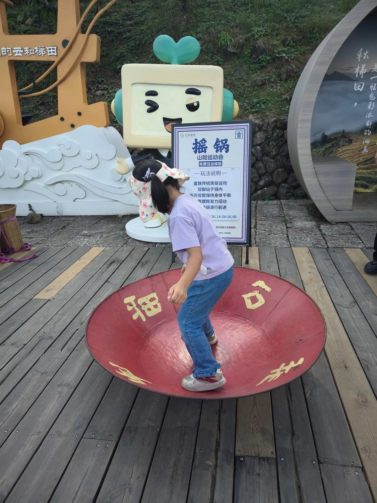 小女孩站在红色圆盘上，旁边立着摇锅的说明牌和卡通立牌