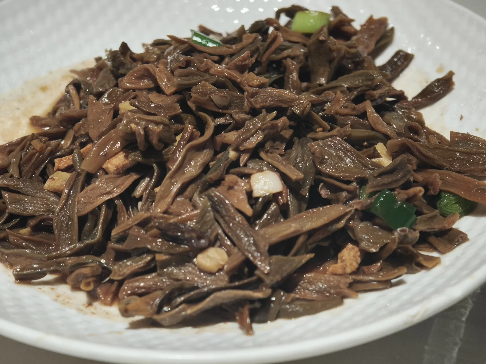 一盘深褐色的干豆角炒菜，泛着油光