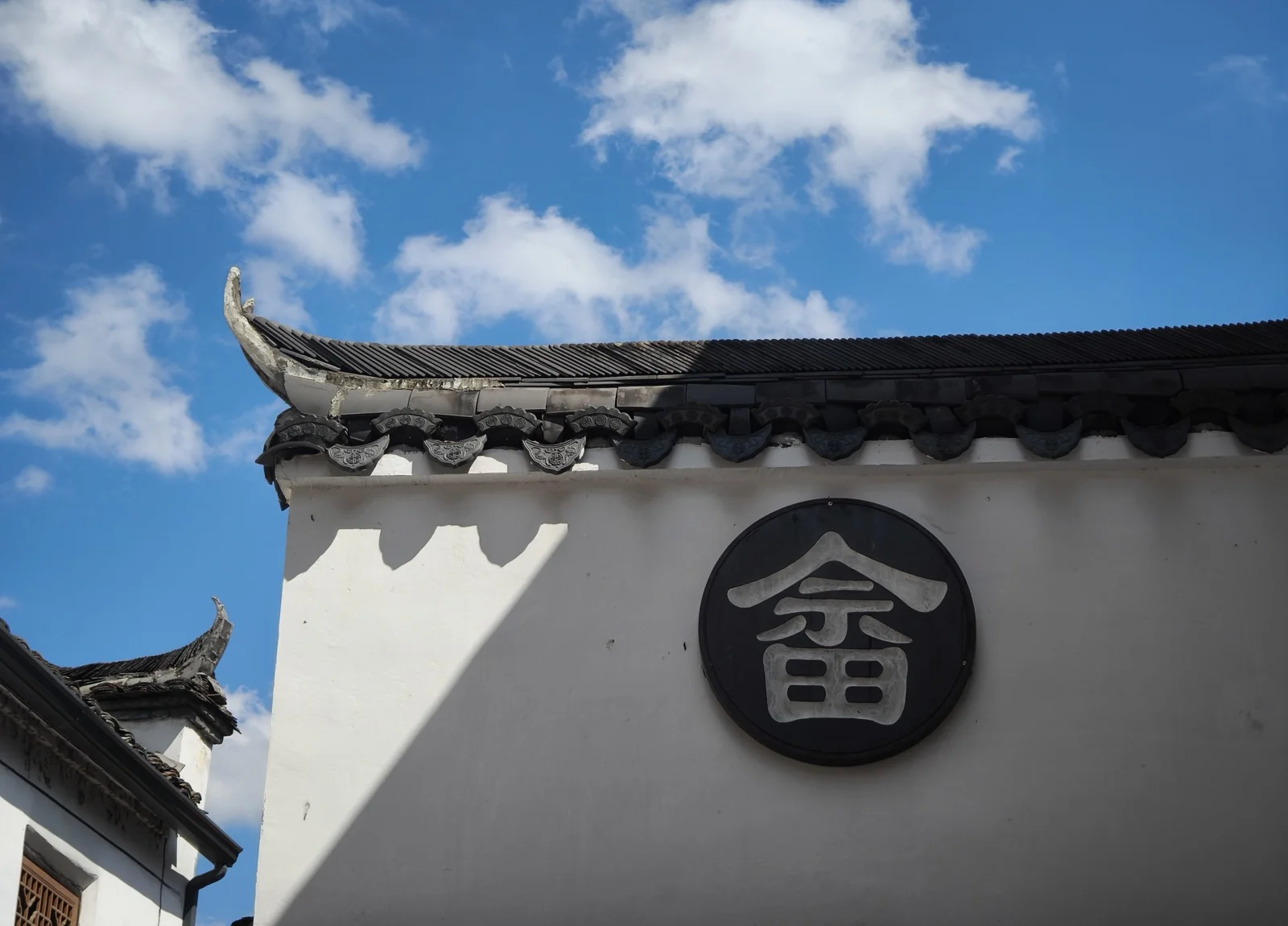 白墙上的黑底圆形牌匾，中间一个畲字，墙头是带滴水瓦的翘角屋檐