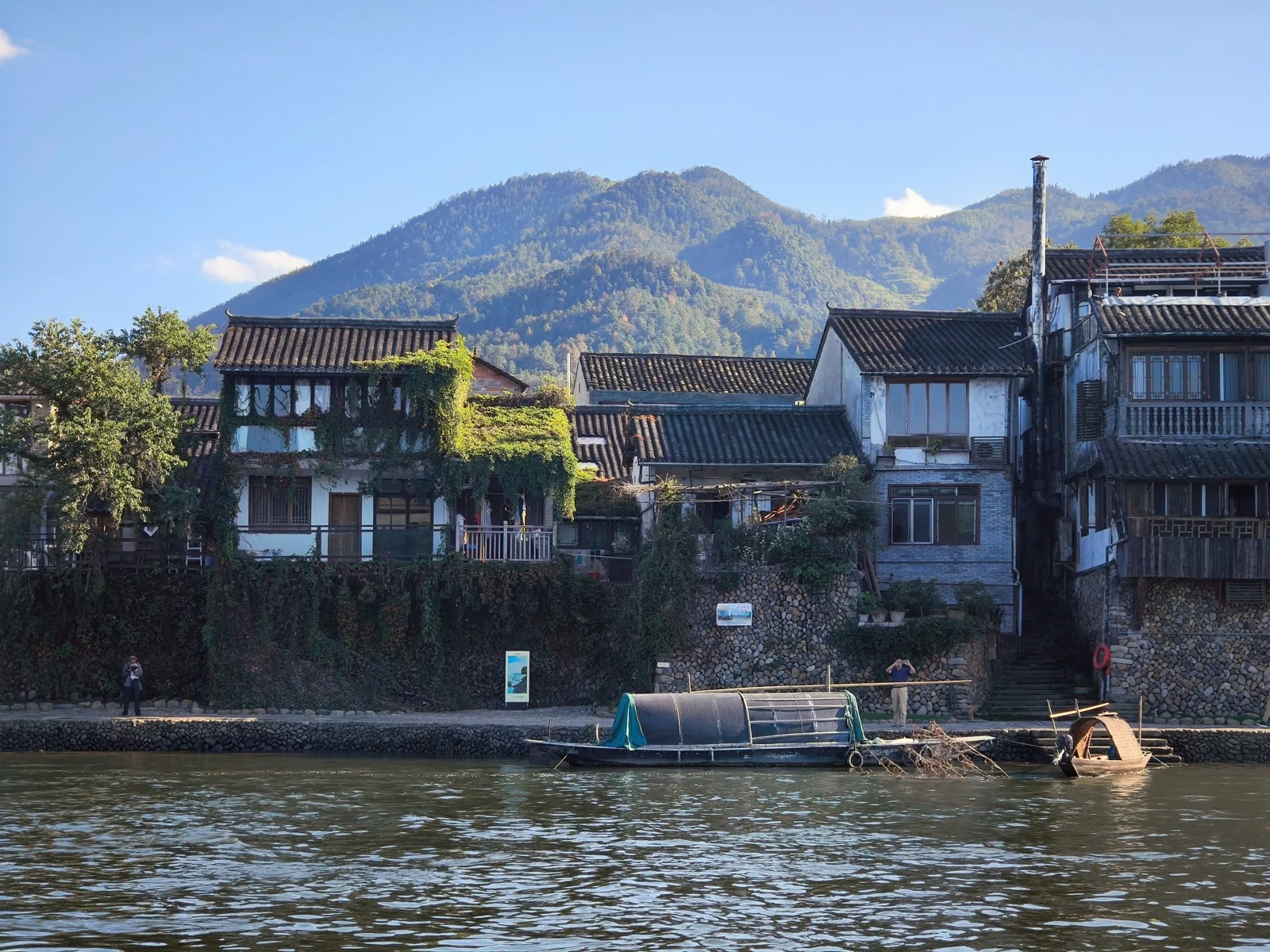 沿江的白墙民房与停泊的小船，背后是青山