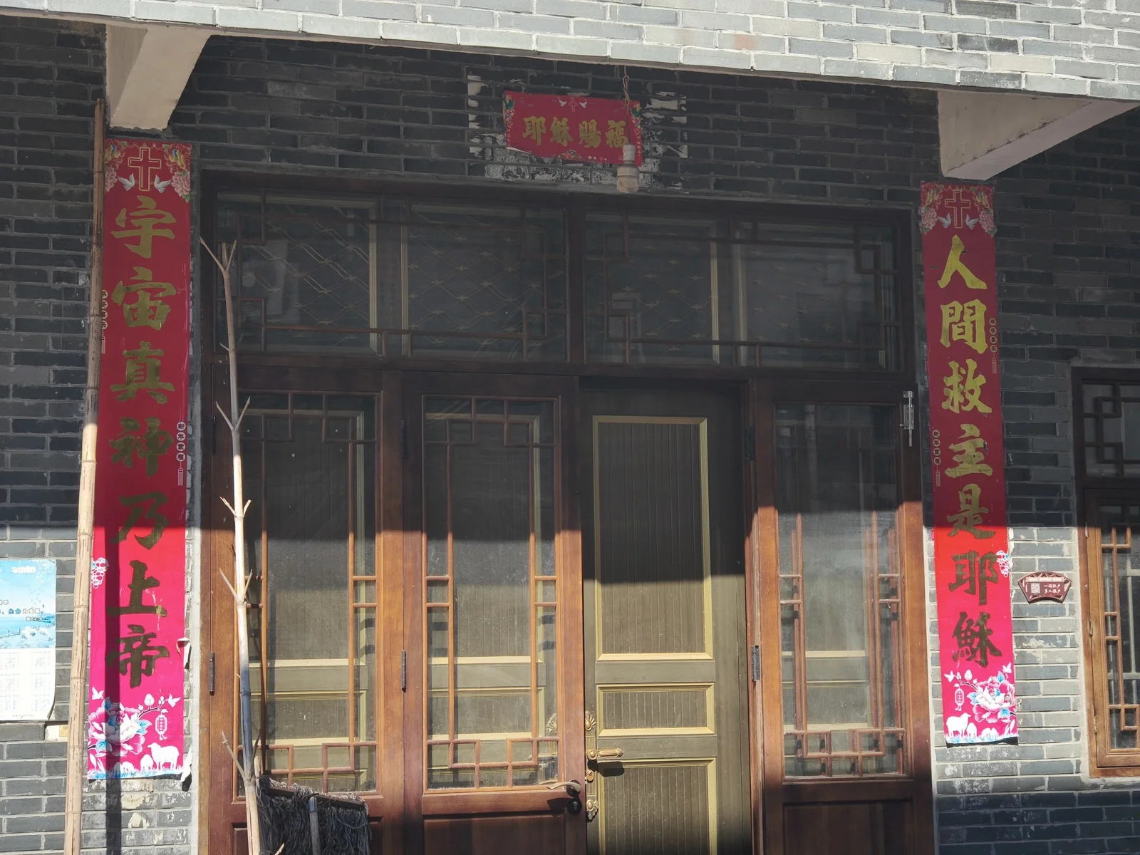 砖墙木门两侧贴着红色基督教对联，门上是红底横批