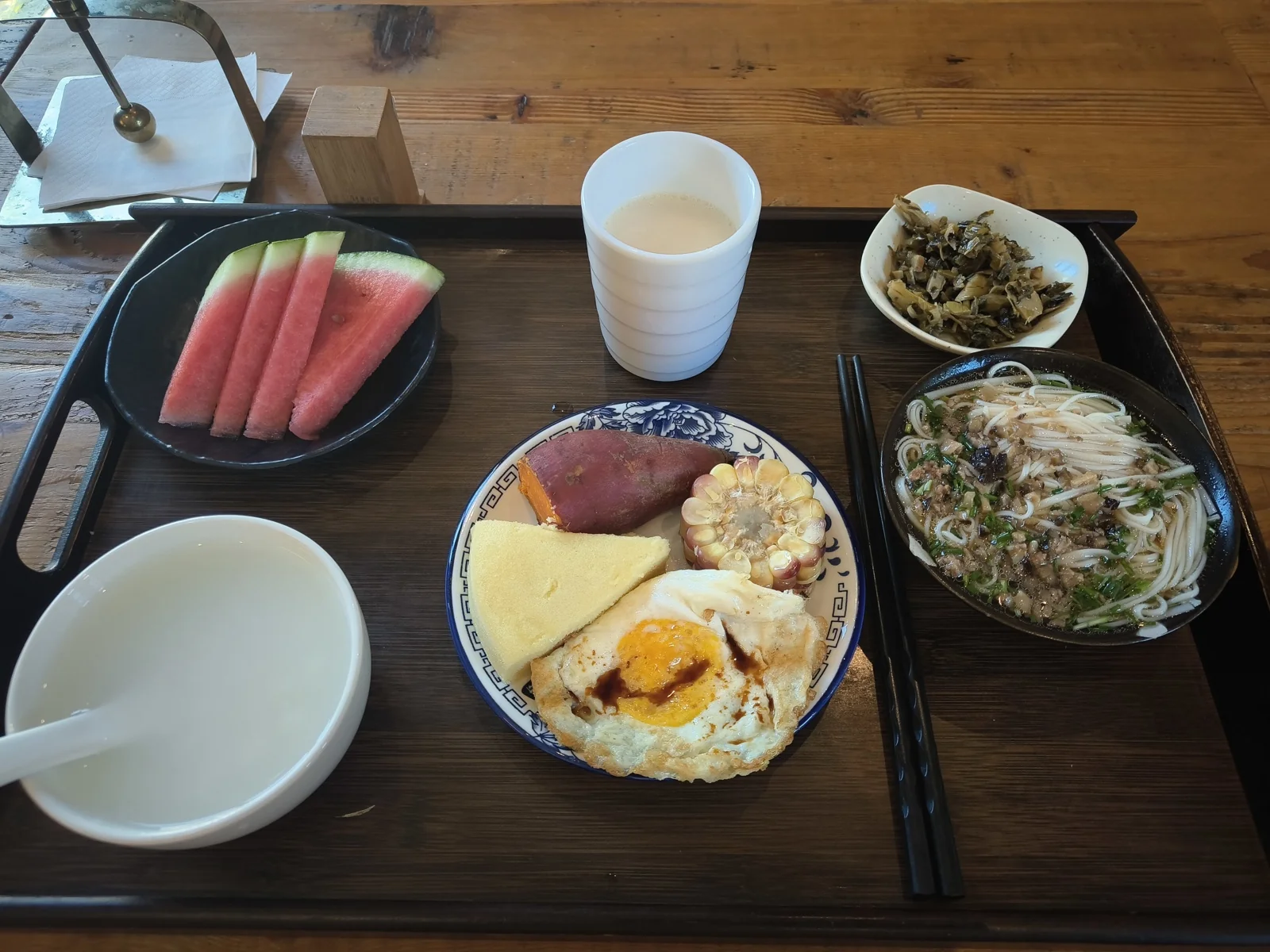 木托盘上的早餐，有米粉、煎蛋、西瓜、小菜和一碗豆浆