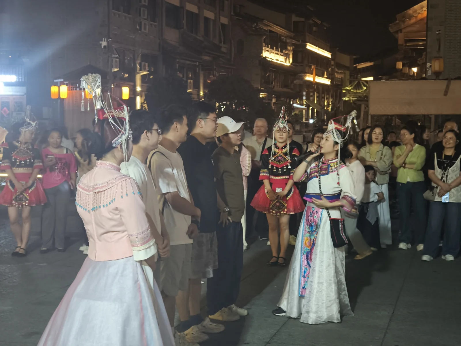 夜色中的畲乡风情街，穿民族服饰的演员被举手机的游客围住