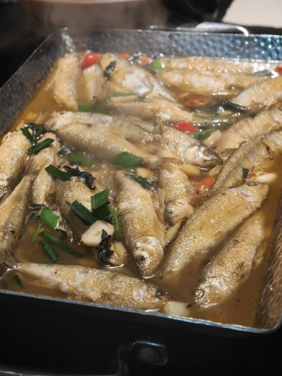 长方铁盘里码满红烧小溪鱼，汤汁里漂着葱花和辣椒