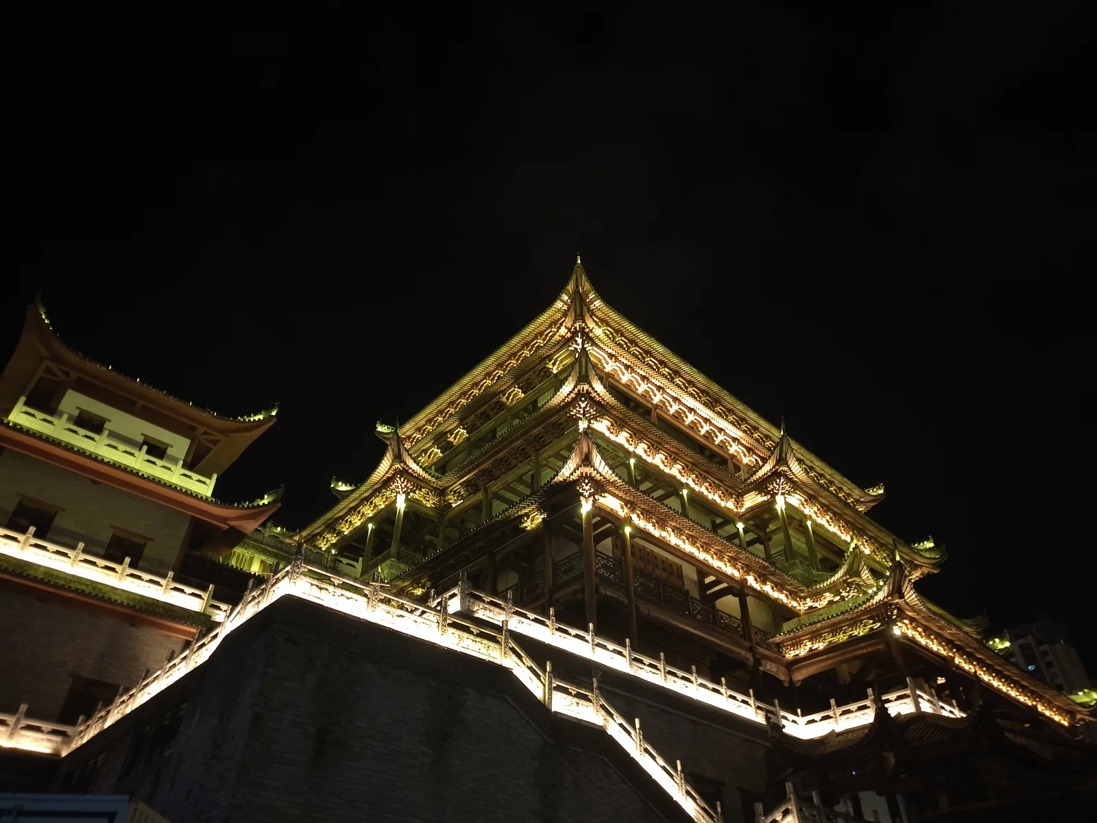 夜色中被灯光照亮的仿古楼阁，层层飞檐沿石砌台基向上收拢