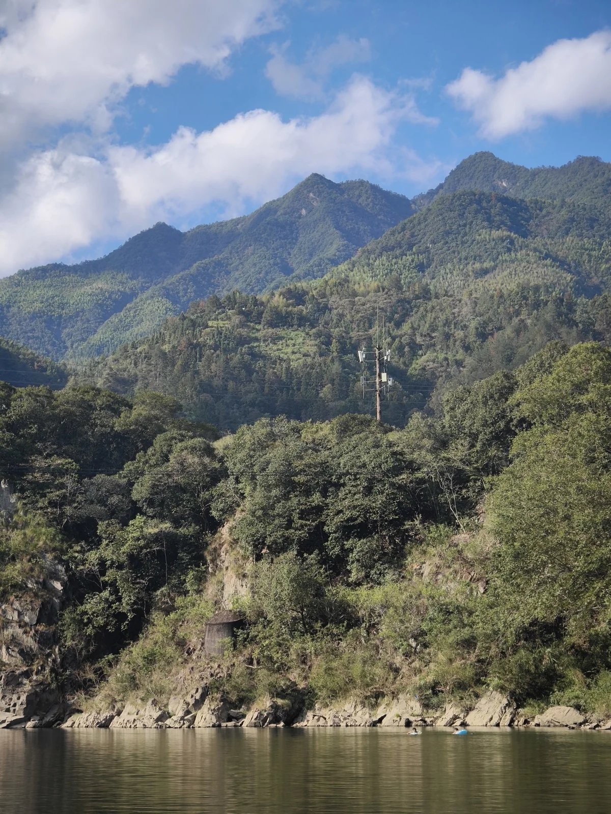 溪对岸林木覆盖的山坡，坡上立着一座通信铁塔，山脚有石砌小棚